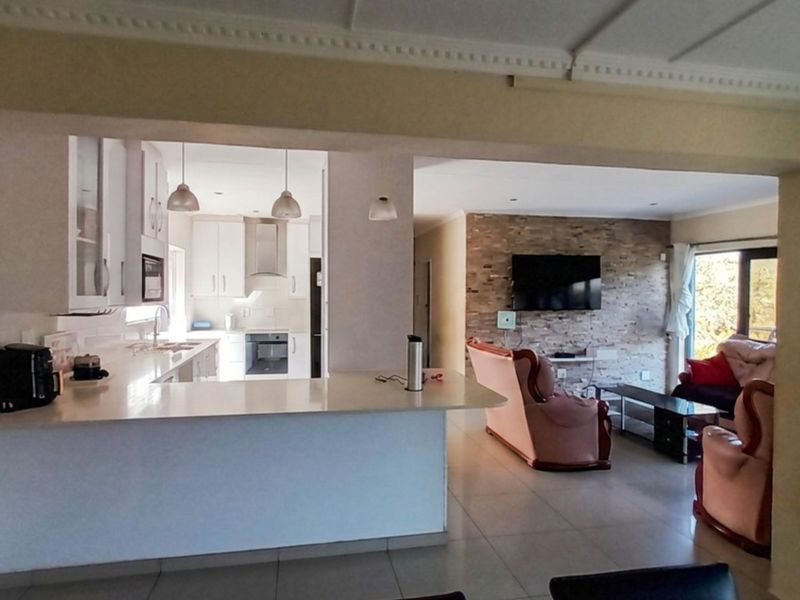 Open-plan living area featuring a modern kitchen with a breakfast bar, stone feature wall, and tiled flooring throughout.