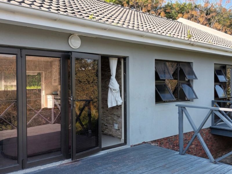 Rear exterior view featuring a timber deck, aluminium stacker doors, and top-hung windows with a brick and plaster facade.