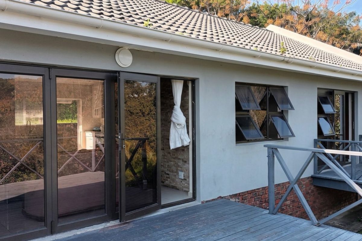 Rear exterior view featuring a timber deck, aluminium stacker doors, and top-hung windows with a brick and plaster facade.