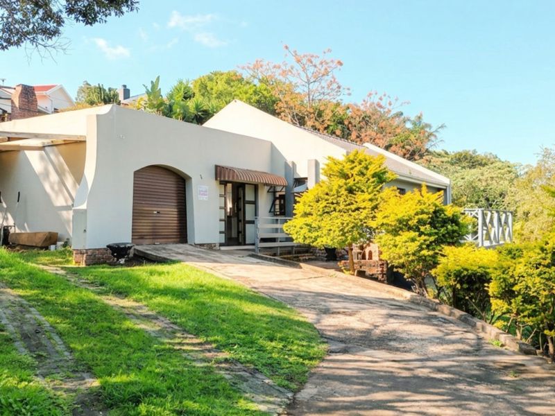 Front exterior view of the house featuring a concrete driveway, roller garage door, and established garden surroundings.