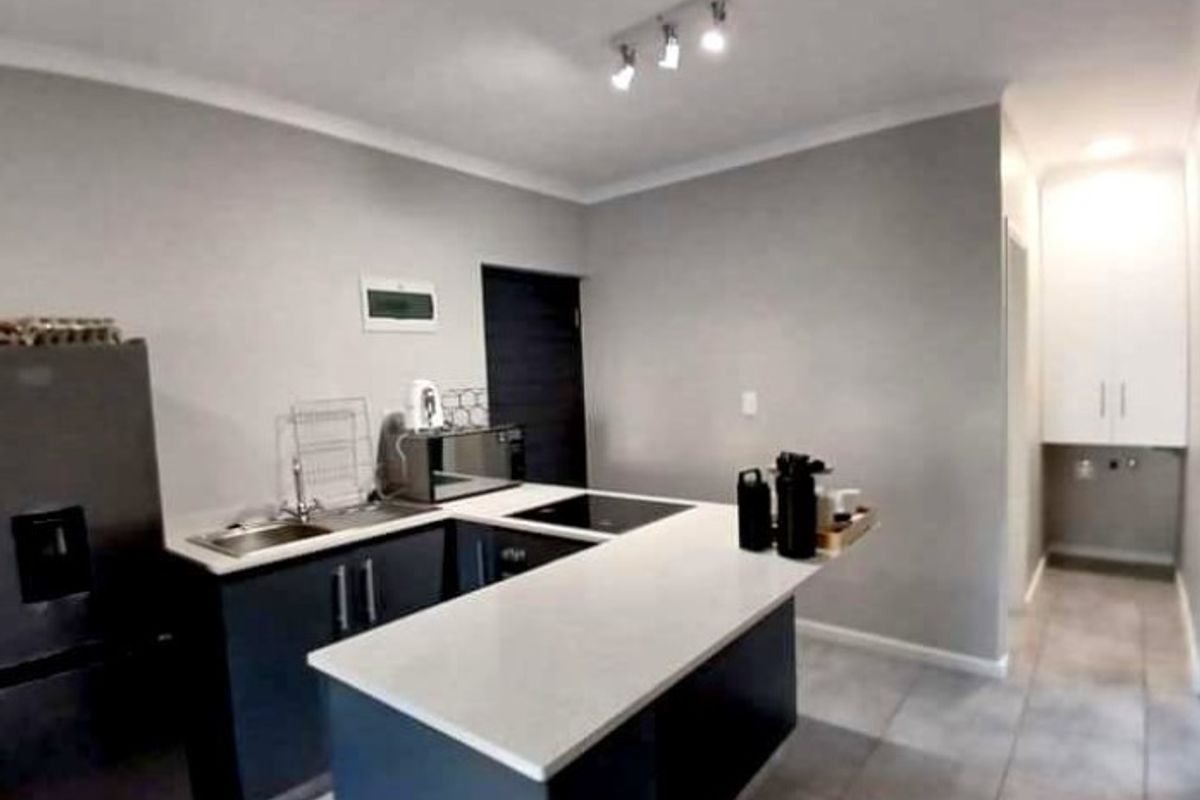 Modern kitchen featuring dark cabinetry, stone countertops, integrated hob, and a breakfast bar, with adjacent utility area and tiled flooring.