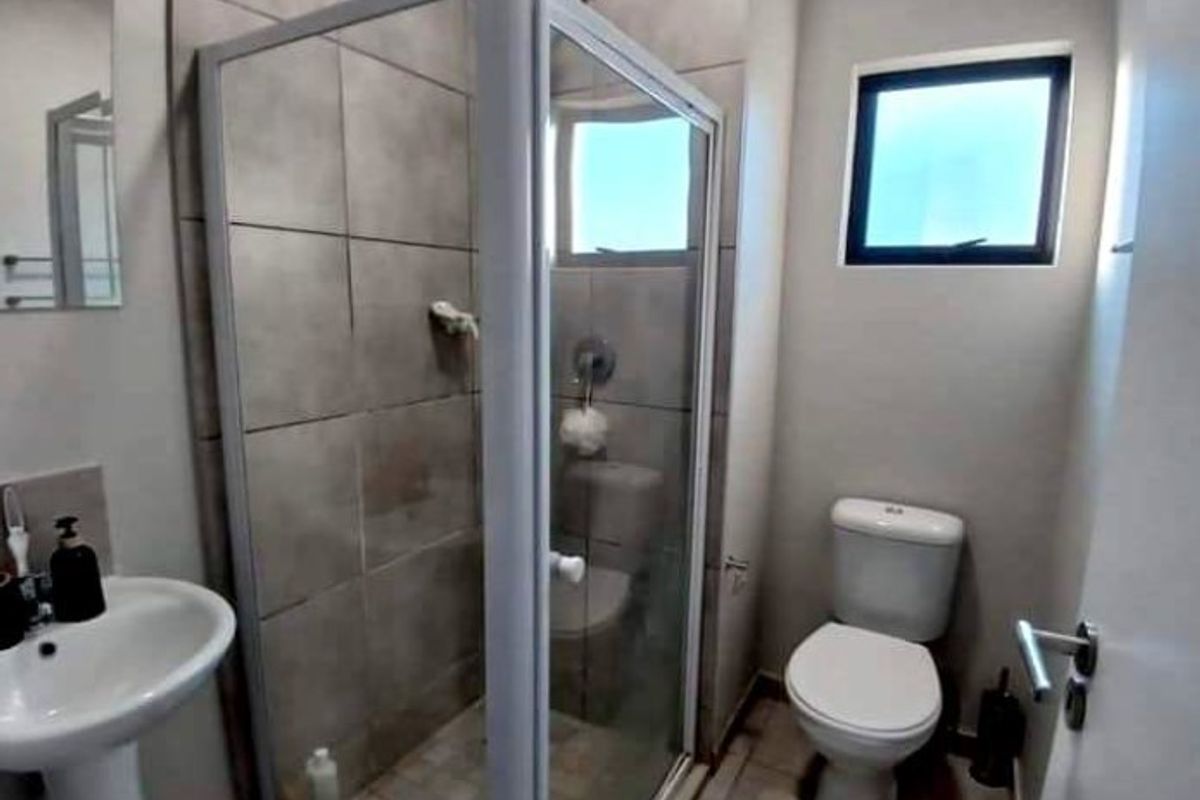 A clean, functional bathroom featuring a glass-enclosed shower, pedestal basin, and toilet with neutral wall and floor tiling.