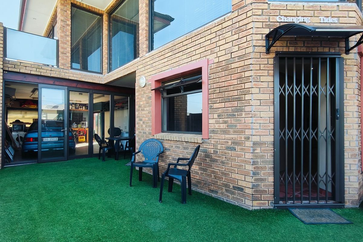 Rear exterior view featuring face brick construction, artificial lawn, aluminium sliding doors leading to a garage space, and a secure entrance with a metal gate.