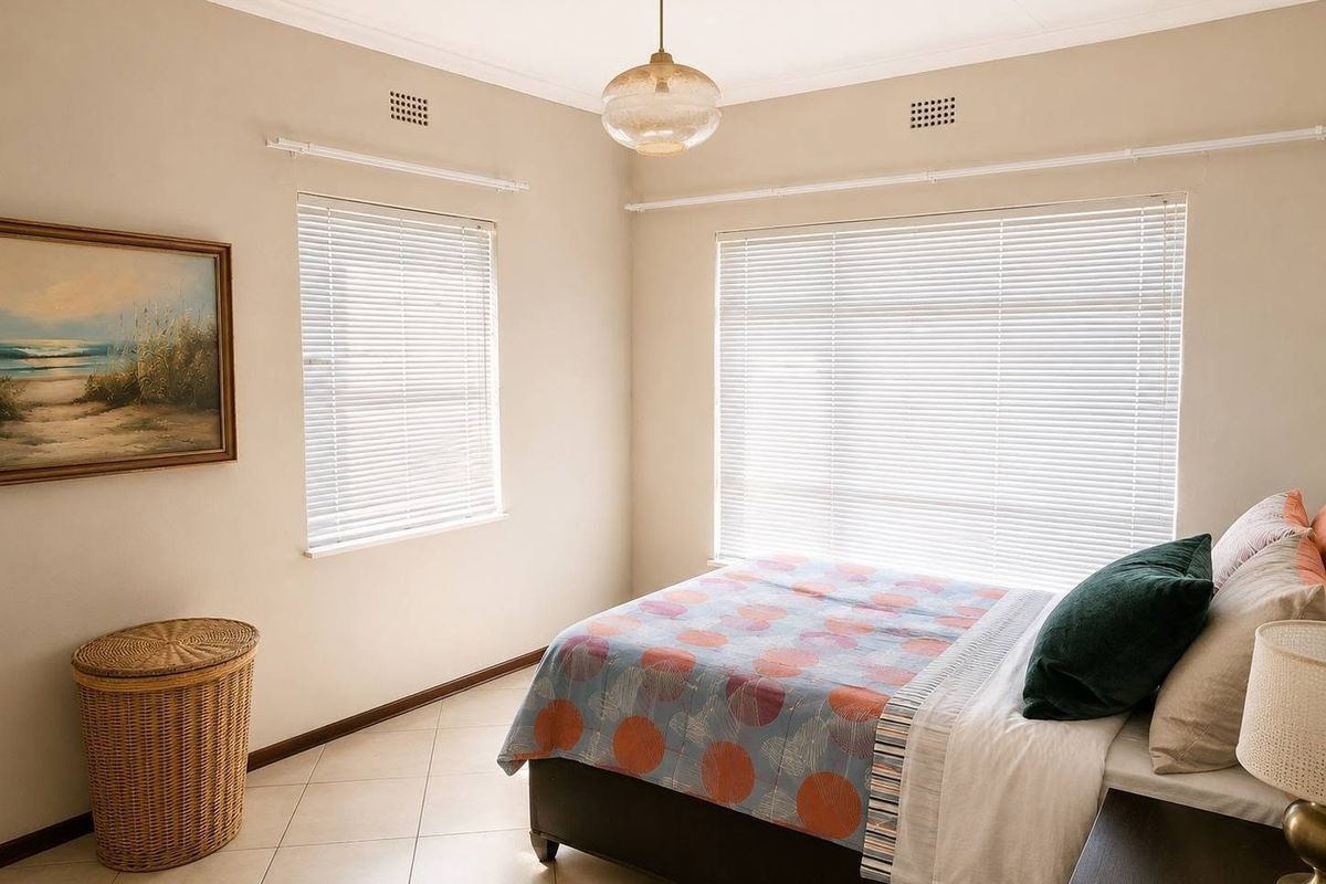 A bright and well-maintained bedroom featuring neutral walls, tiled flooring, and dual windows fitted with venetian blinds.