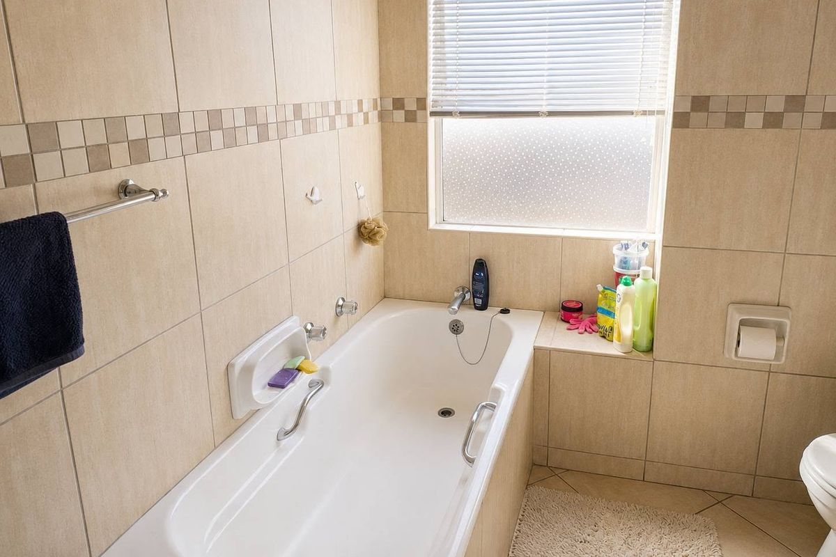A functional bathroom featuring a built-in bathtub with chrome fixtures, tiled wall finishes, and a window with a venetian blind.