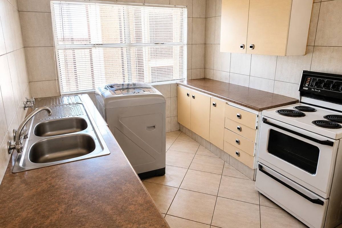 A functional kitchen featuring tiled walls and flooring, laminate countertops, double bowl sink, and built-in cabinetry with a freestanding electric stove.