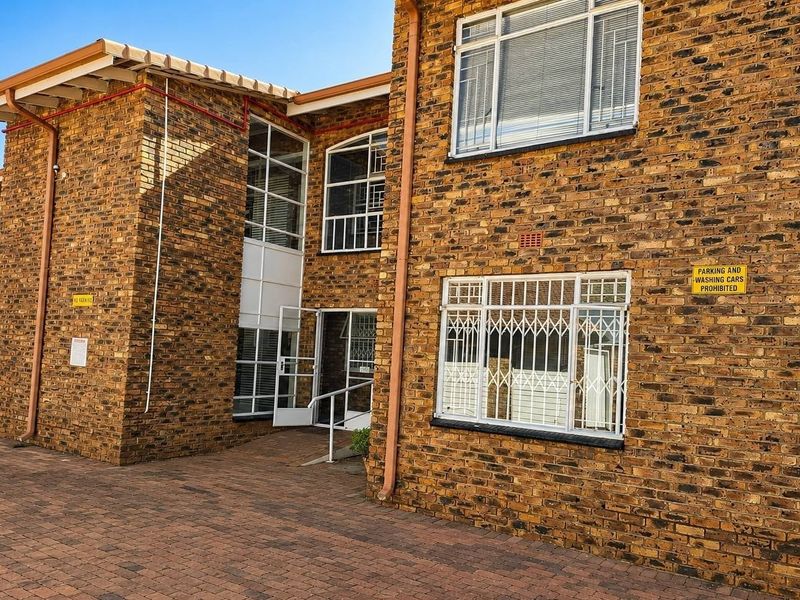 Exterior view of a face brick apartment building featuring paved driveway access and secure window bars.