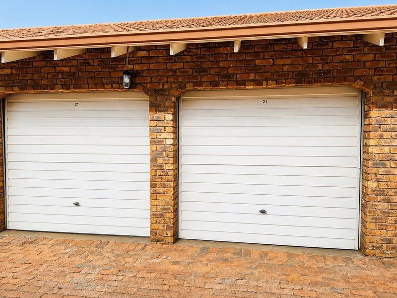 A well-maintained double garage featuring white sectional doors, exposed brickwork, and a tiled roof, set above a paved driveway.