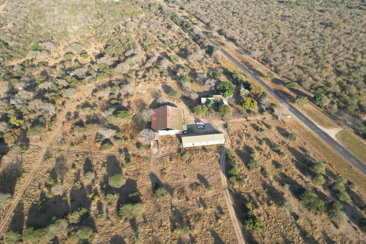 Aerial view of a rural farm property featuring multiple outbuildings, a corrugated metal roof, and surrounding natural landscape with access to a main road.