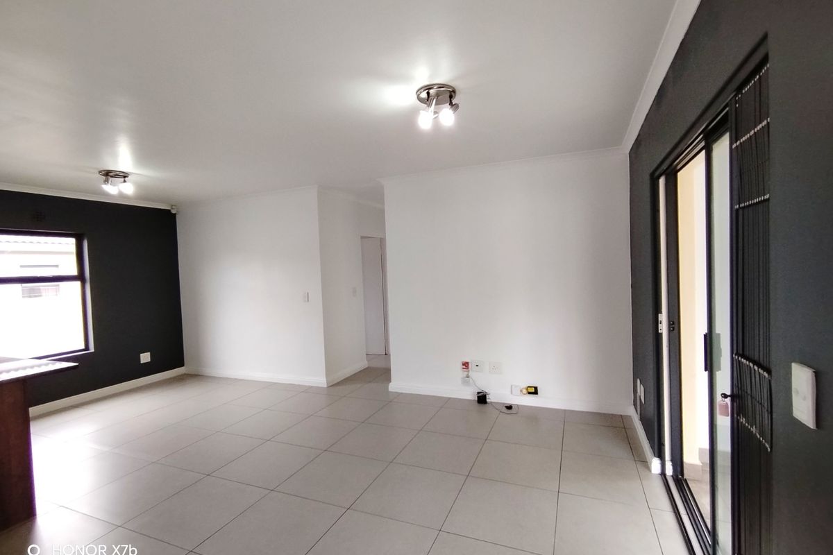 A bright, empty living area featuring neutral tiled flooring, modern dark accent walls, and sliding glass doors providing access to the exterior.