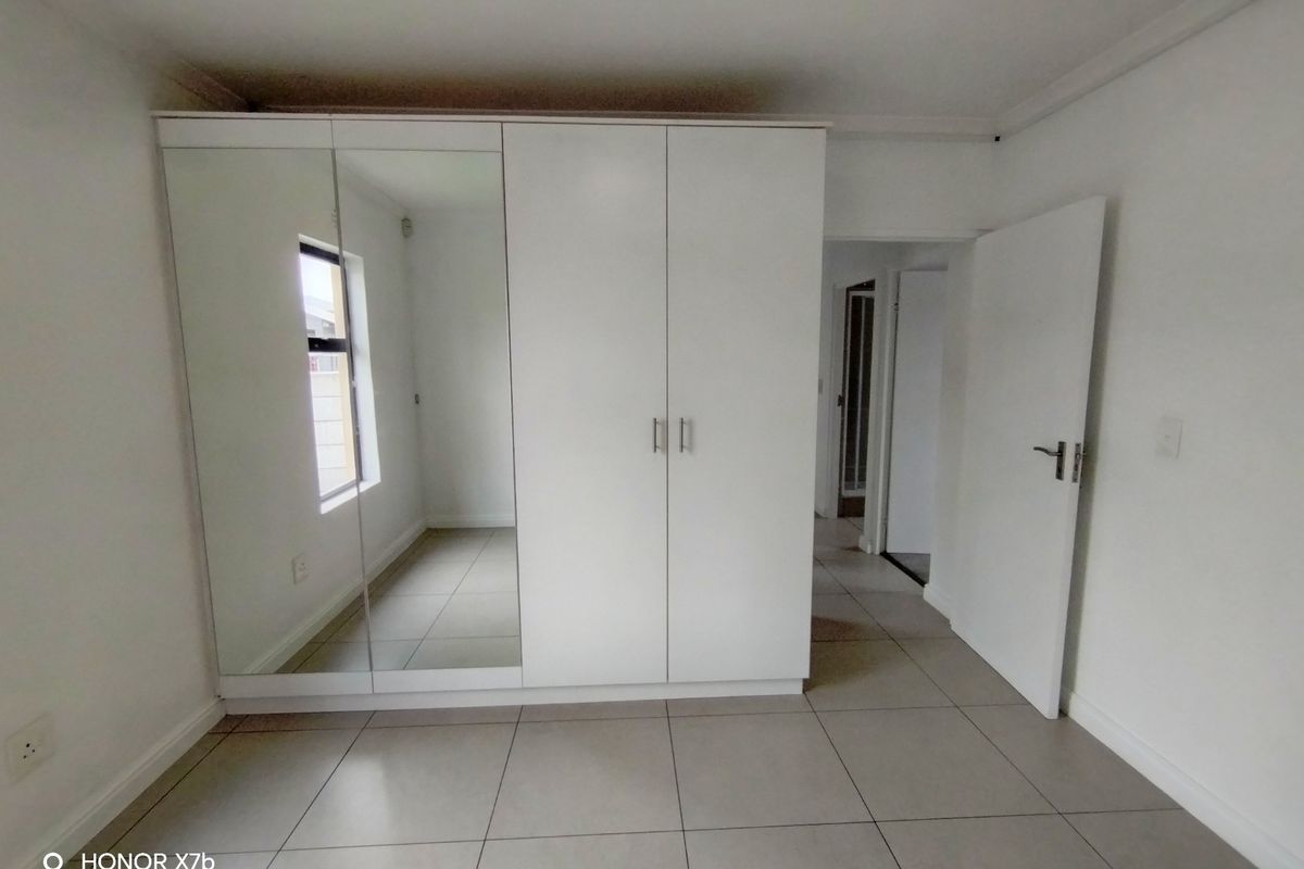 A clean, empty bedroom featuring neutral tiled flooring and a large, modern built-in wardrobe with mirrored panels.