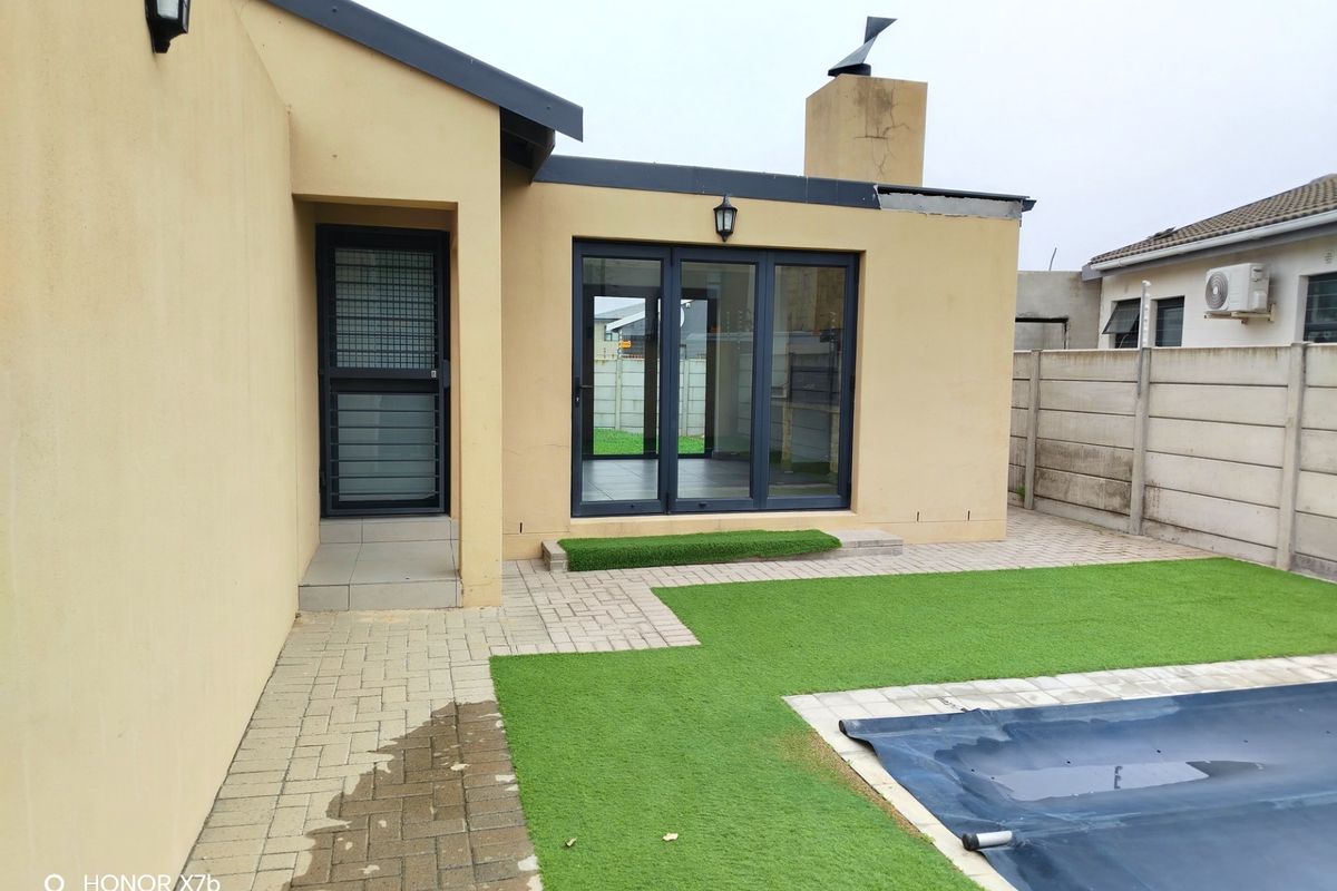 Rear exterior view featuring a paved patio area, artificial lawn, swimming pool with cover, and access to the home via sliding glass doors.