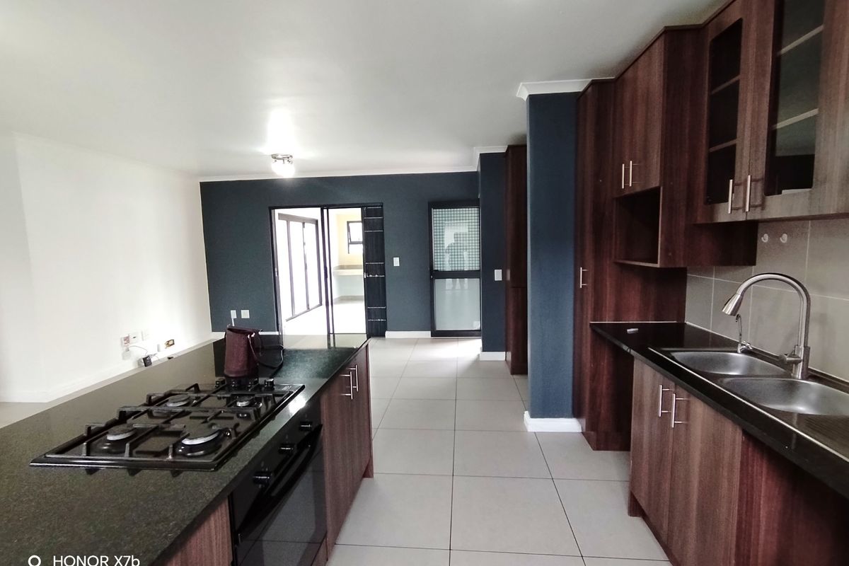 Modern kitchen featuring dark wood cabinetry, granite countertops, a central island with a gas hob, and tiled flooring, leading to an adjacent living area.