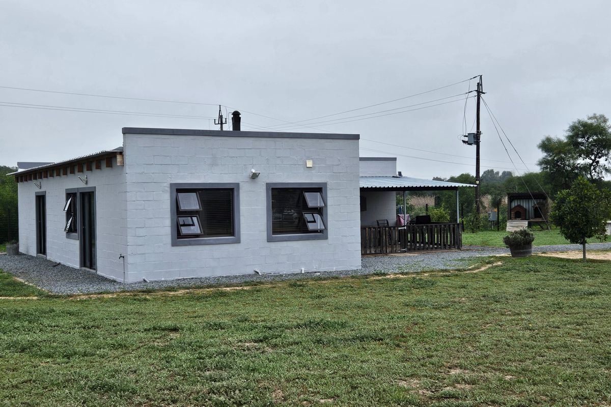Rear view of a modern concrete block dwelling featuring a covered patio area and low-maintenance gravel landscaping on a small holding.