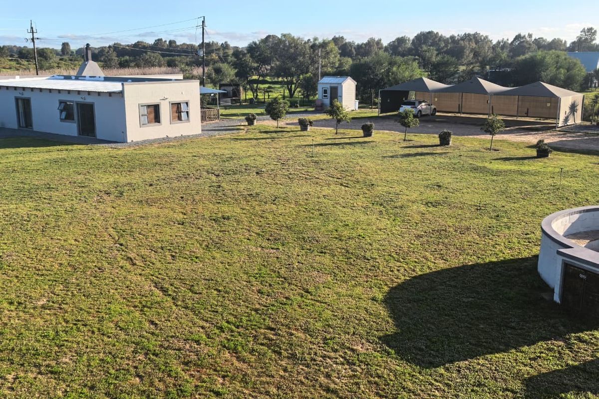 Aerial view of a spacious small holding featuring a main dwelling, a carport, and a large, well-maintained lawn area.