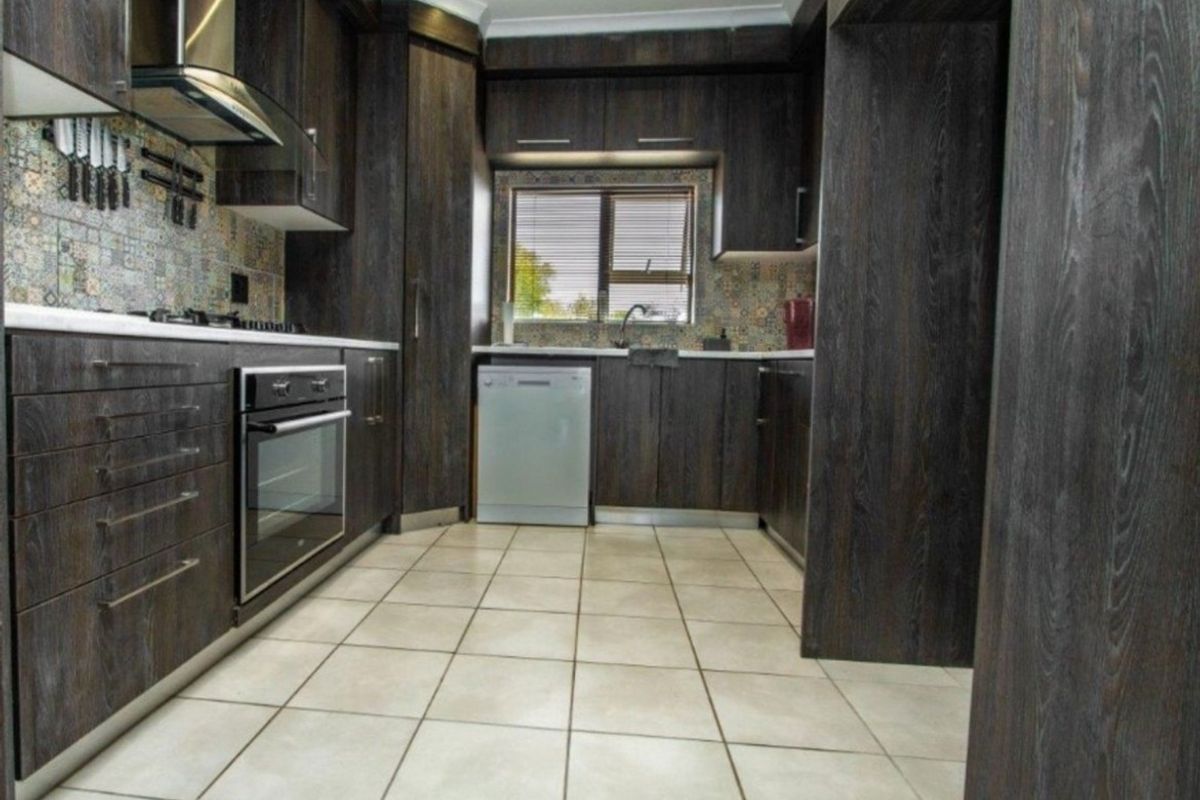 Modern kitchen featuring dark wood cabinetry, mosaic tile backsplash, built-in oven, extractor fan, and tiled flooring with ample storage space.