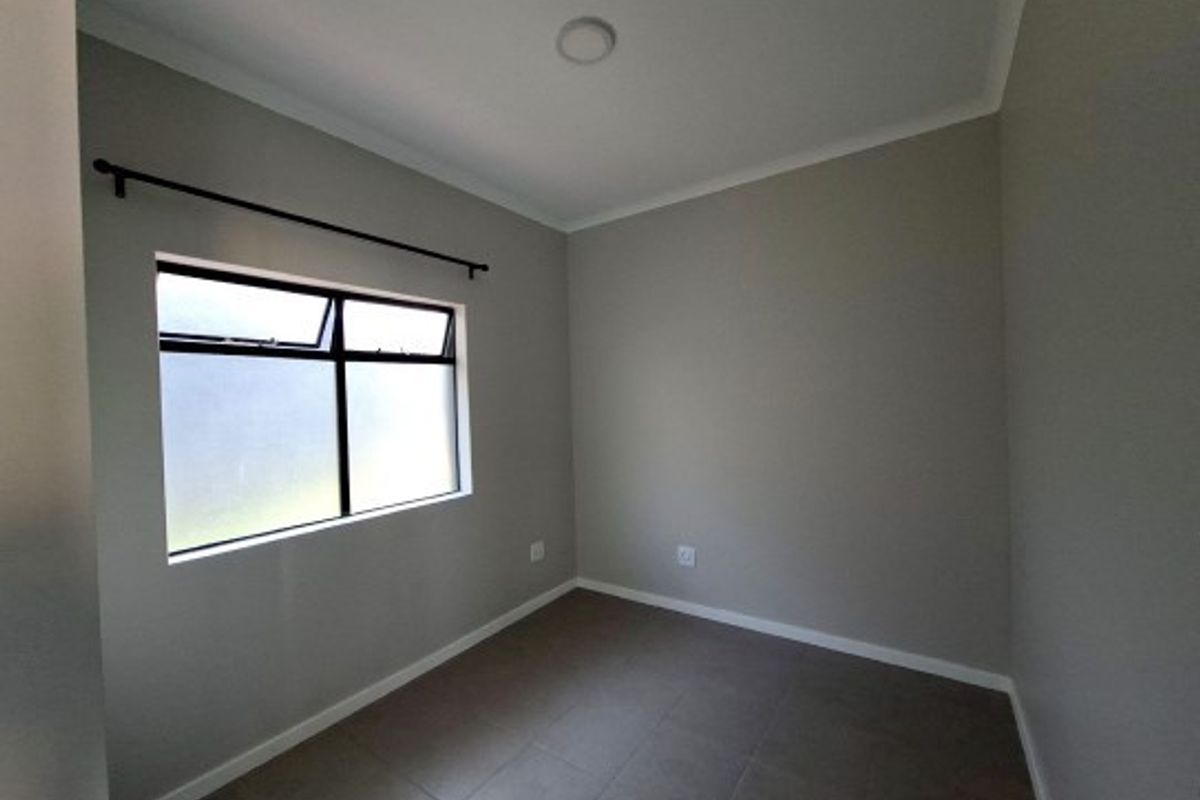 A clean, empty bedroom featuring neutral grey walls, tiled flooring, and a frosted glass window with a fitted curtain rod.