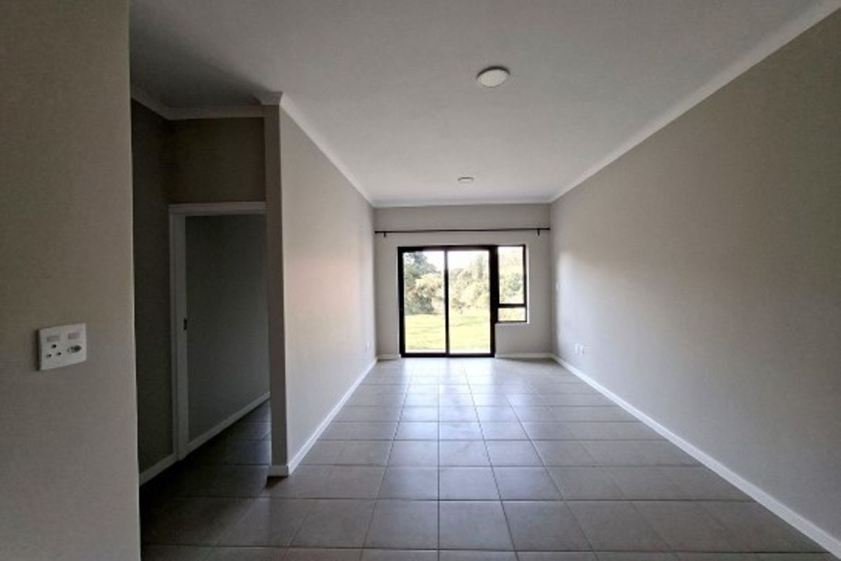 A spacious, empty living area featuring neutral tiled flooring, coved cornicing, and a large sliding glass door providing natural light and outdoor access.