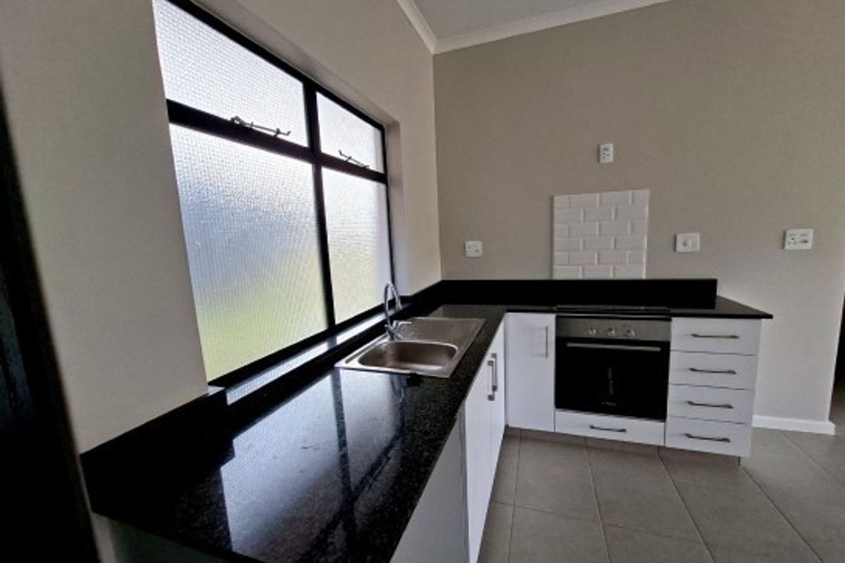 A clean, modern kitchen featuring granite countertops, white cabinetry, a built-in oven, and a subway tile backsplash with tiled flooring.