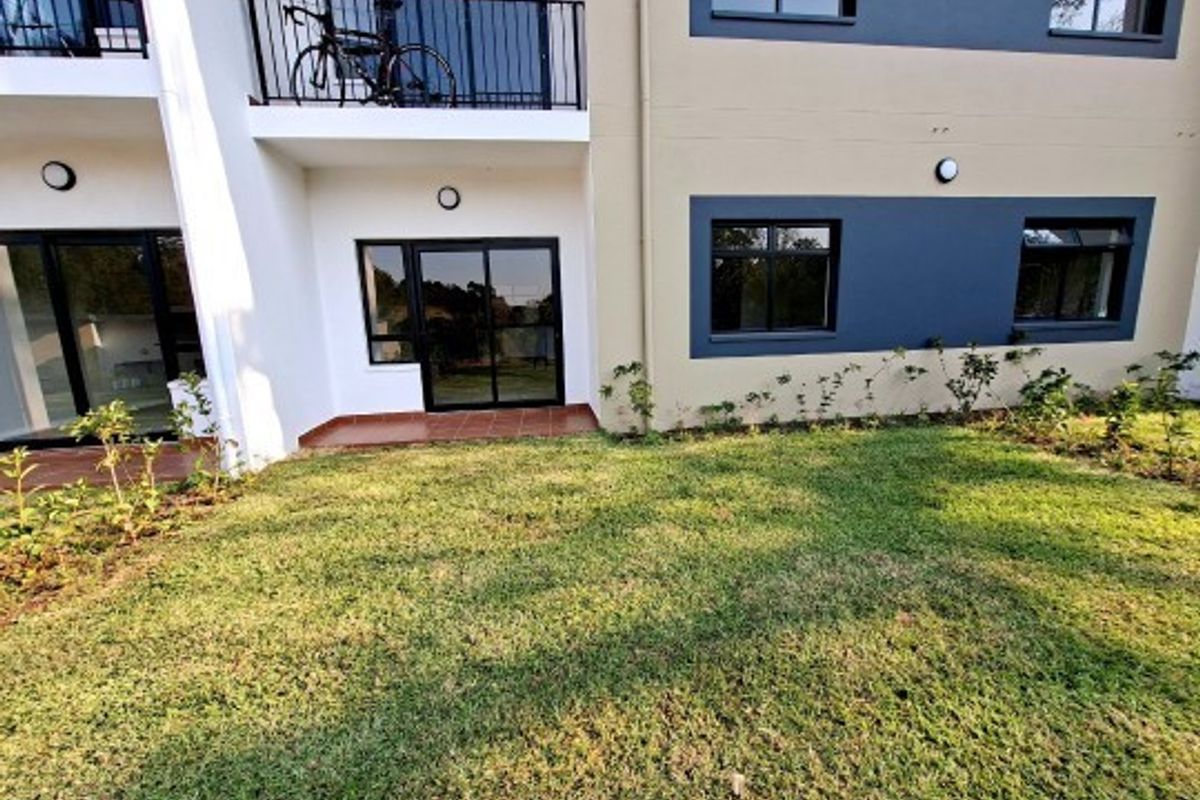 Rear view of the apartment building featuring a ground floor patio, a first-floor balcony with metal railings, and a private garden area.