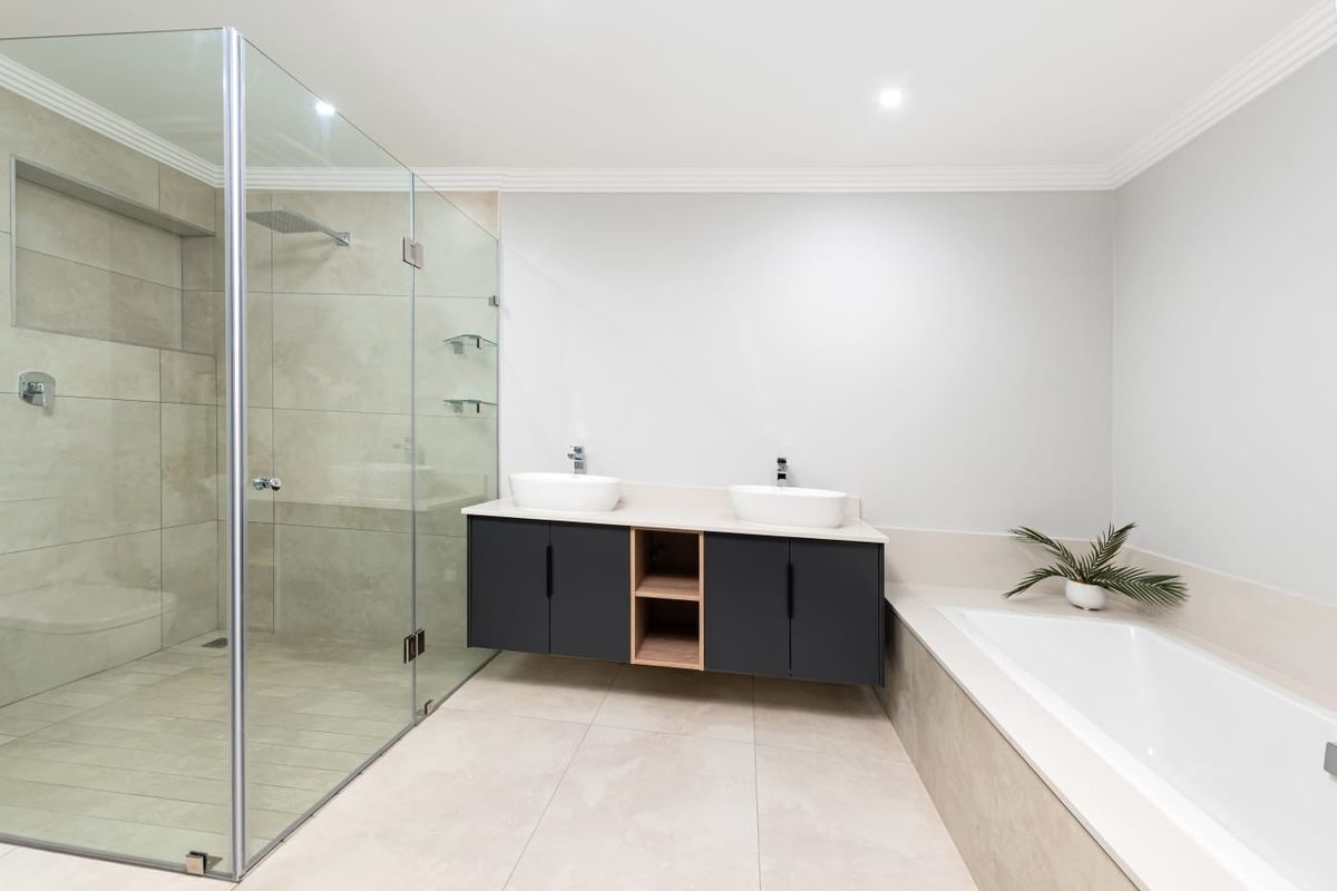 Modern bathroom featuring a frameless glass shower, double vanity with vessel sinks, and a built-in bathtub with neutral tile finishes.