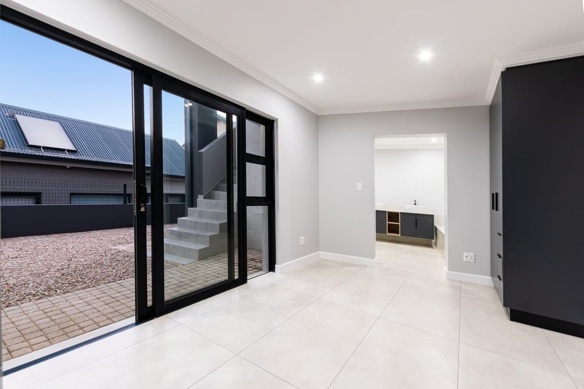 A bright, modern bedroom featuring large sliding glass doors leading to an outdoor area, tiled floors, and built-in cupboards with an en-suite bathroom.