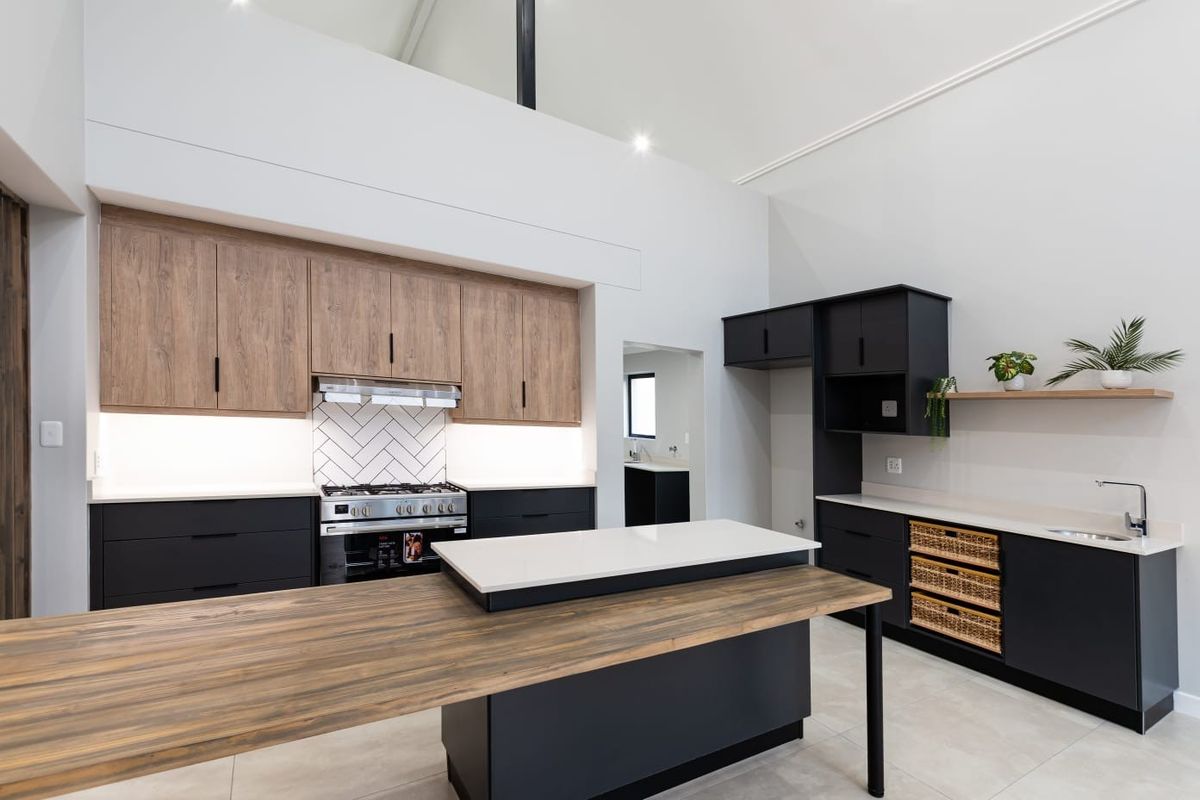 Modern kitchen featuring two-tone cabinetry, stone countertops, a central island with breakfast bar, gas stove, and a striking herringbone tile backsplash under vaulted ceilings.