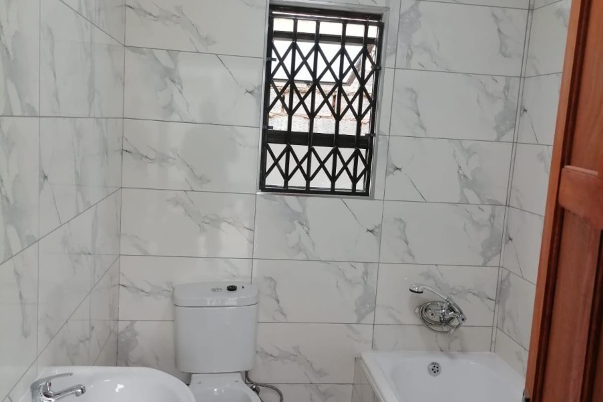 A clean, modern bathroom featuring marble-look wall tiles, a pedestal basin, a standard toilet, and a bathtub with a mixer tap.