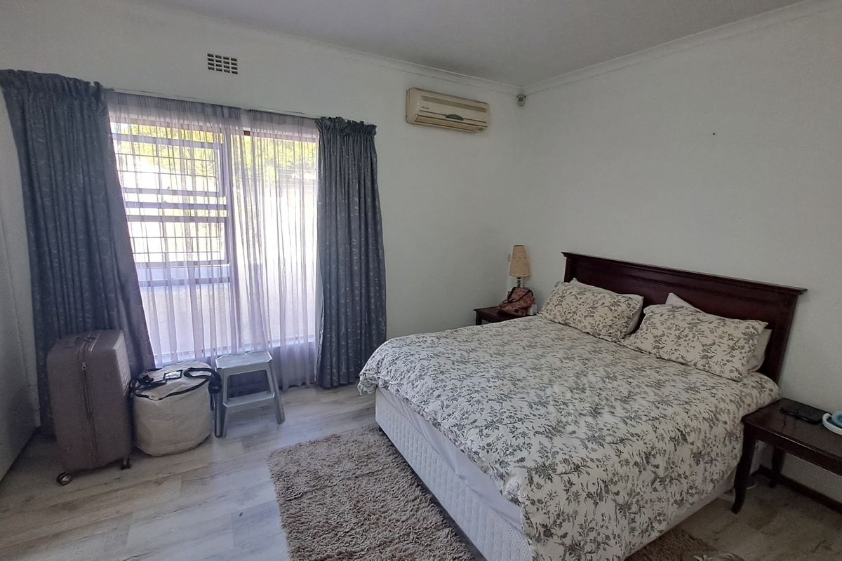 A bedroom featuring laminate flooring, an air conditioning unit, and built-in storage, with security bars installed on the window.