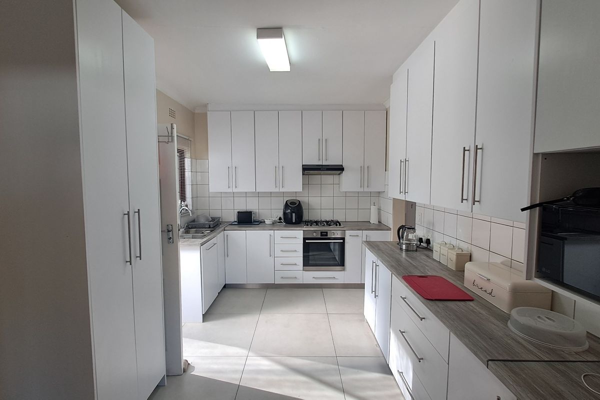 A functional kitchen featuring white cabinetry, built-in oven, gas hob, extractor fan, tiled splashback, and durable tiled flooring.