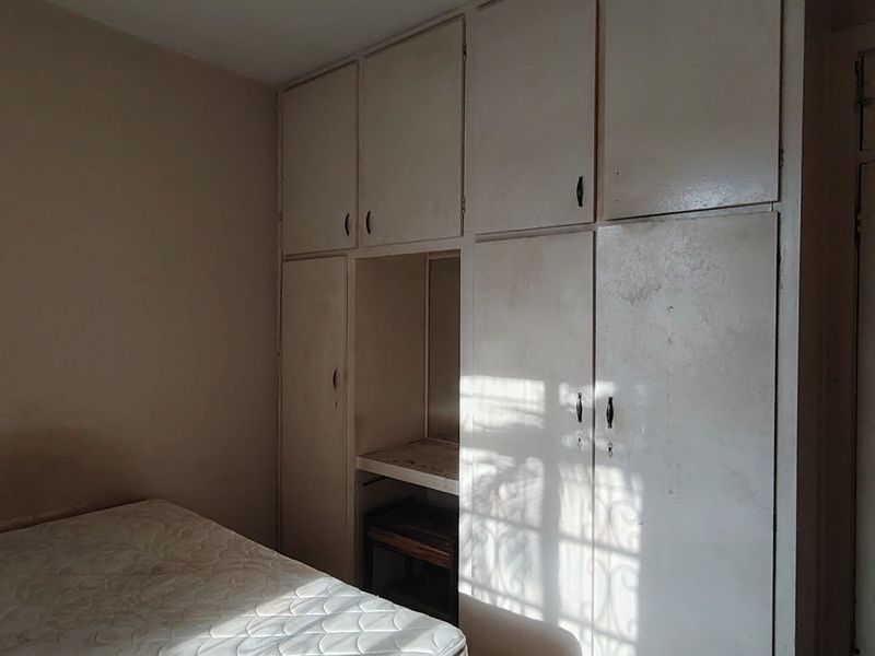 A bedroom featuring extensive built-in cupboard storage and a classic internal door, requiring cosmetic updates to modernize the space.