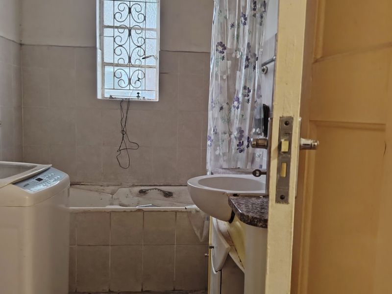 A dated bathroom featuring a bathtub, basin, and tiled walls. The space requires renovation to update the finishes and address visible wear.