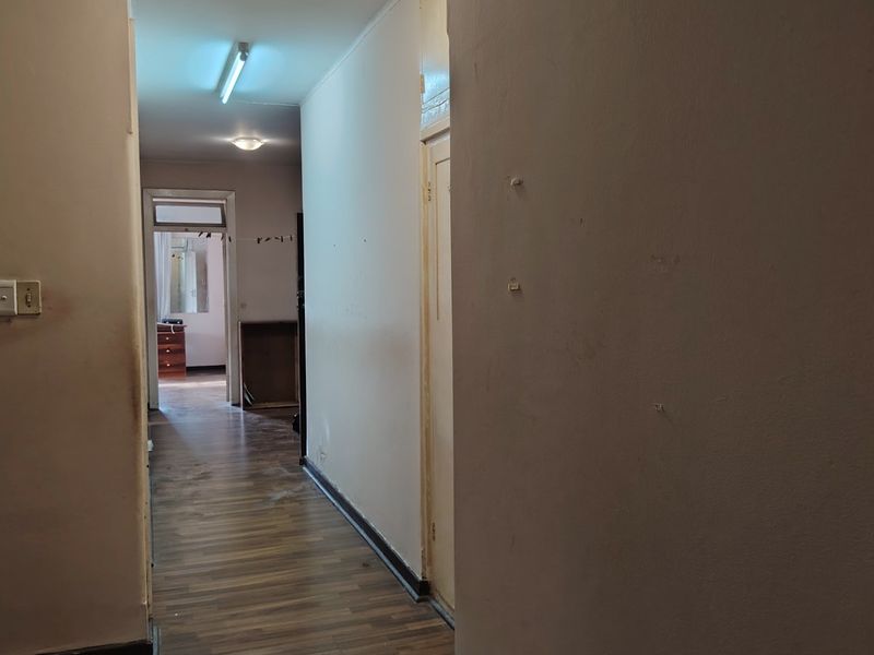 A vacant hallway featuring laminate flooring and basic lighting, showing signs of wear on the walls and floor surfaces.