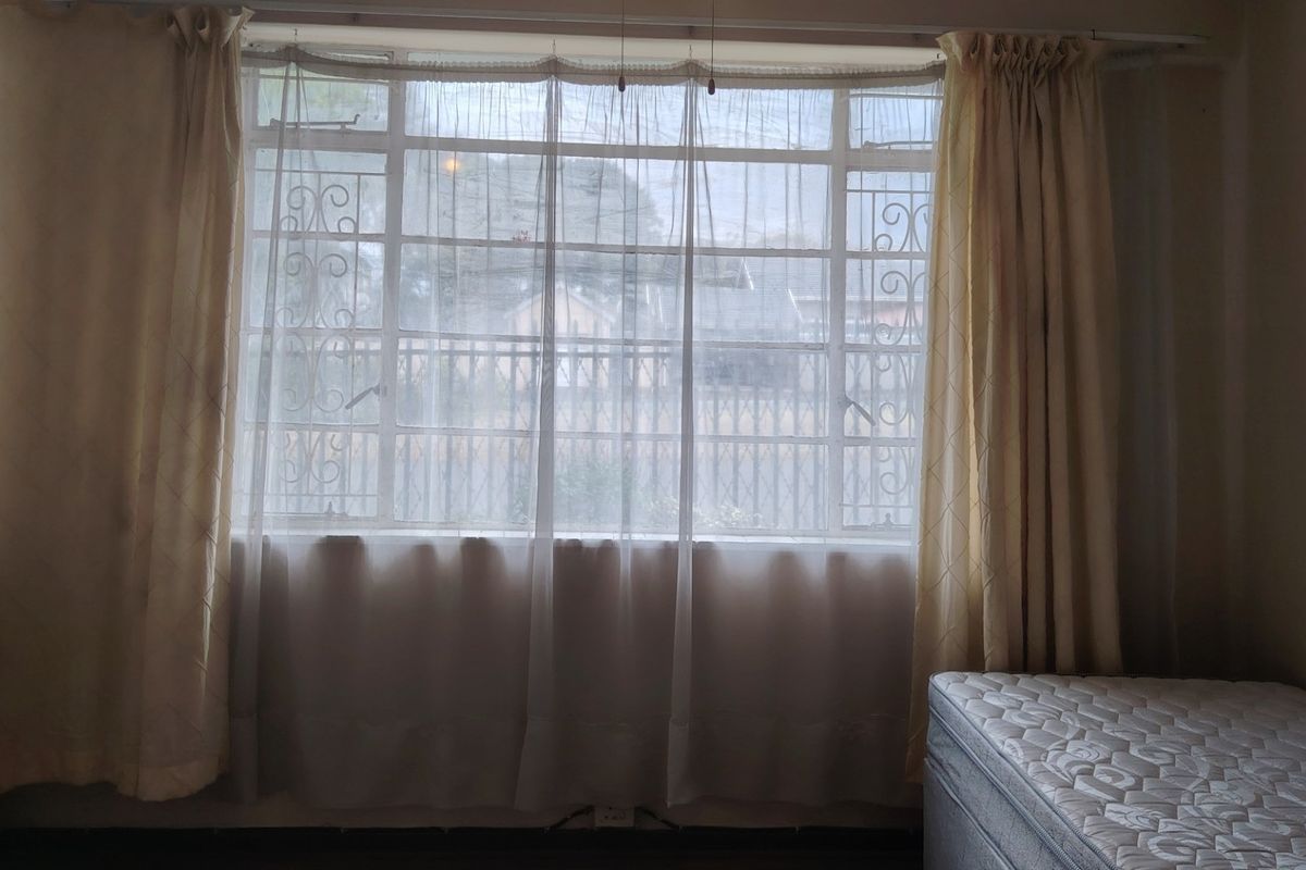 A bedroom featuring a large steel-framed window with integrated security bars, providing natural light and a view of the exterior.