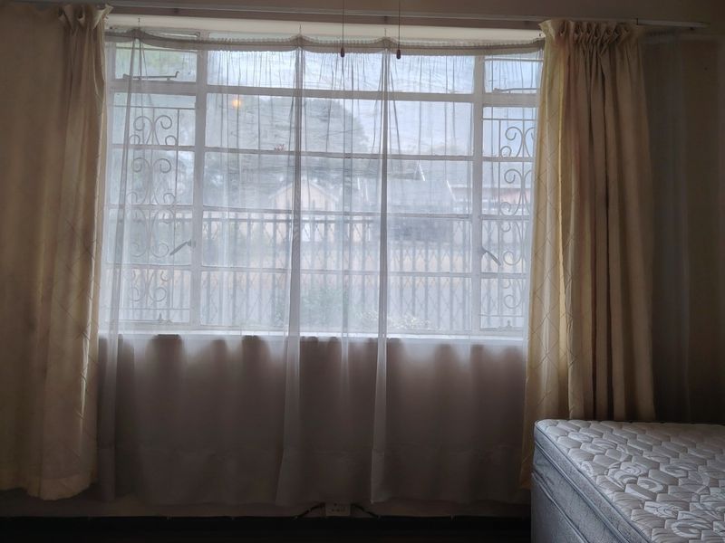A bedroom featuring a large steel-framed window with integrated security bars, providing natural light and a view of the exterior.