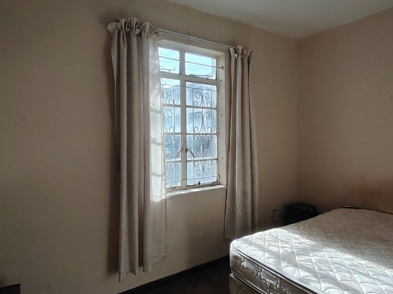 A bedroom featuring a window with security bars and neutral wall finishes, requiring cosmetic updates to improve its overall appeal.