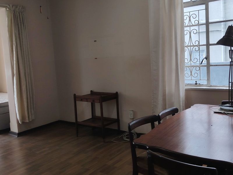 A living area featuring laminate flooring and a window with security bars, showing signs of wear on the walls.