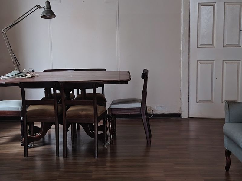 A dining area featuring laminate flooring and a traditional panel door, requiring cosmetic updates to the wall finishes and trim.