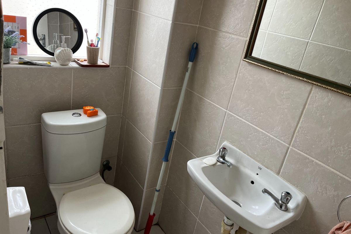 A compact bathroom featuring a wall-mounted basin, toilet, and neutral wall tiling.