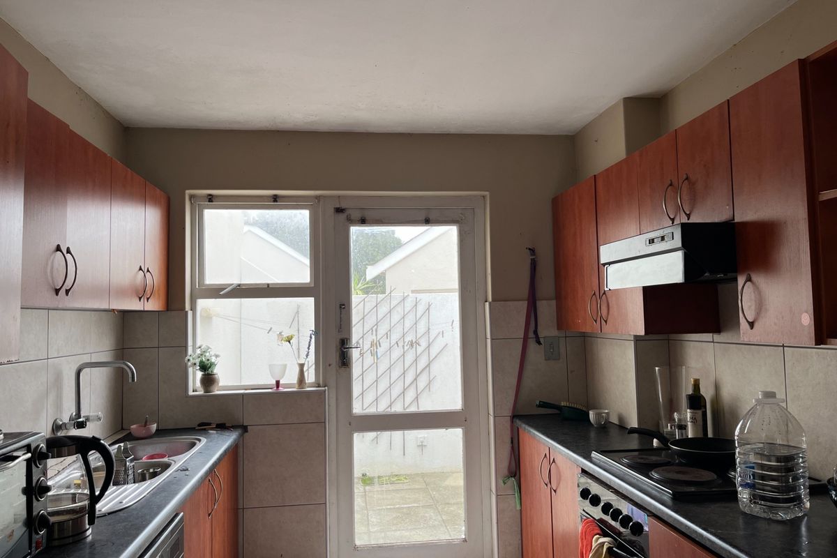 A functional kitchen featuring laminate cabinetry, dark countertops, built-in oven with hob, and direct access to the exterior via a glass-paneled door.