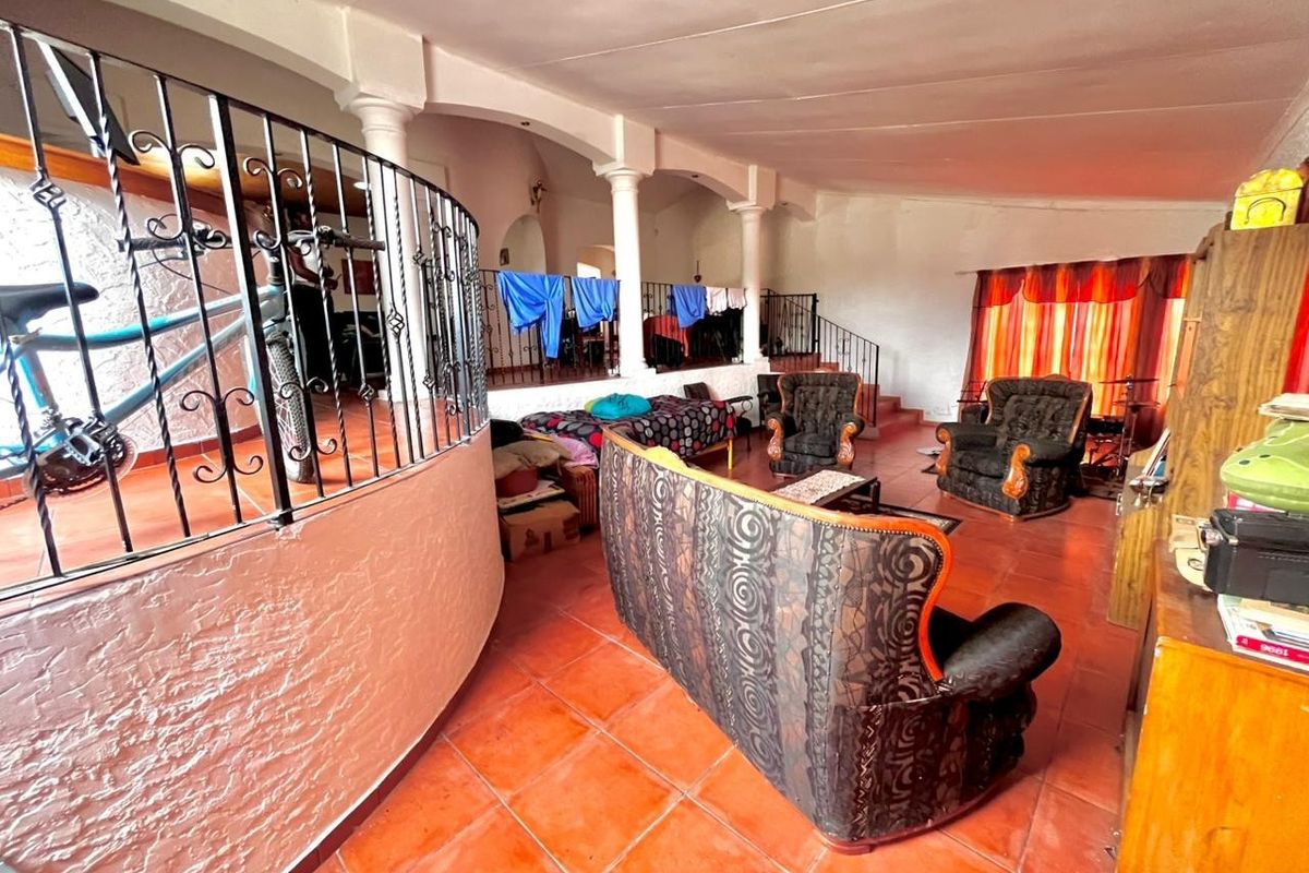 Spacious split-level living area featuring terracotta floor tiles, decorative wrought iron balustrades, and structural columns, offering a unique architectural layout.