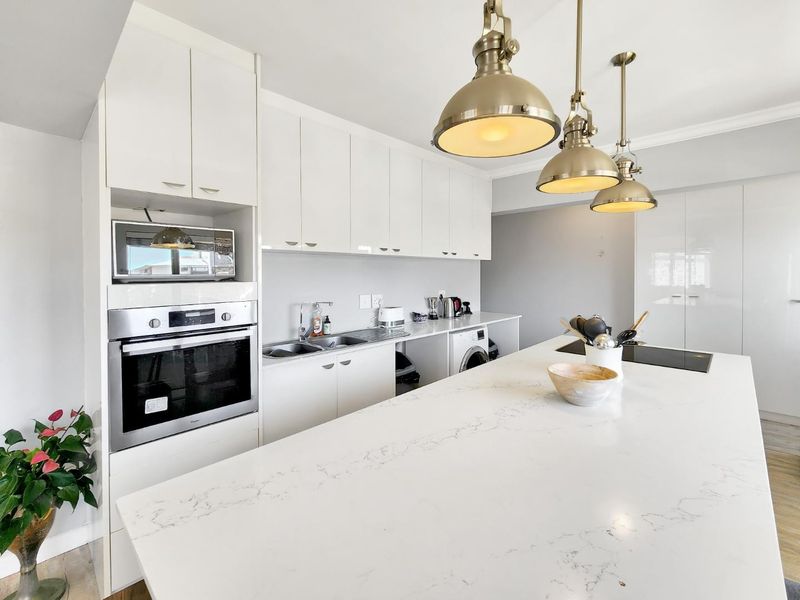 Modern kitchen featuring a large white quartz island, sleek white cabinetry, built-in oven and microwave, and stylish pendant lighting.