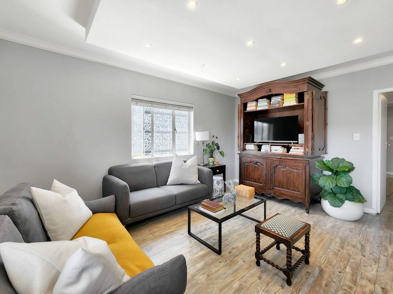 A well-maintained living room featuring recessed downlights, a decorative cove ceiling, and durable laminate flooring.