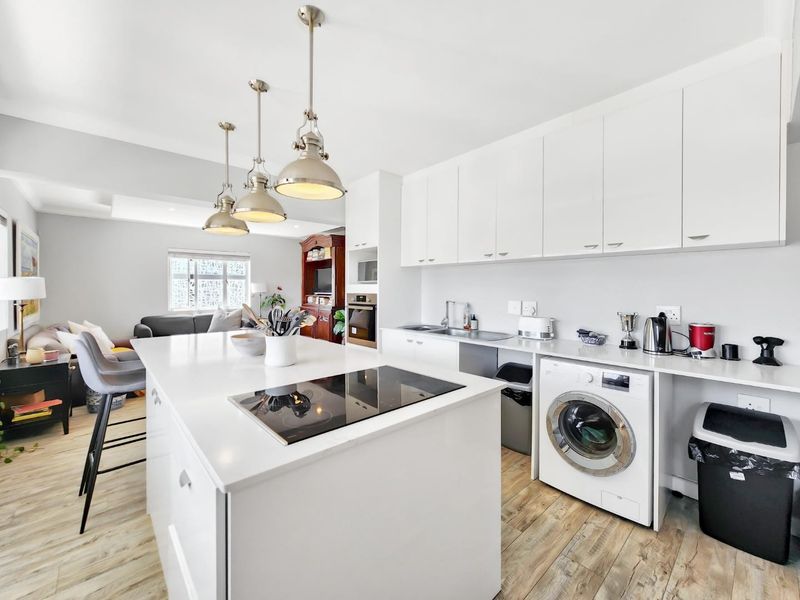 Modern open-plan kitchen featuring a central island with induction hob, sleek white cabinetry, integrated appliances, and wood-look laminate flooring.