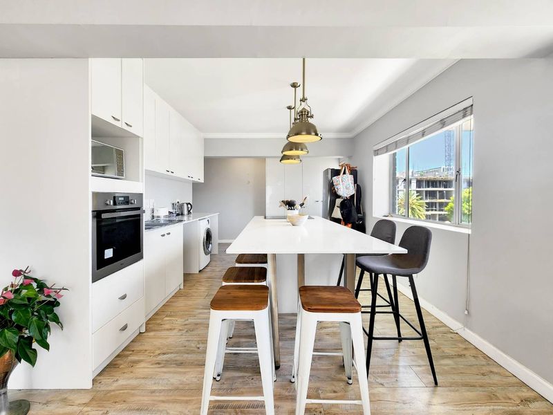 Modern kitchen featuring white cabinetry, a central island with breakfast bar seating, built-in oven, microwave, and integrated laundry facilities.