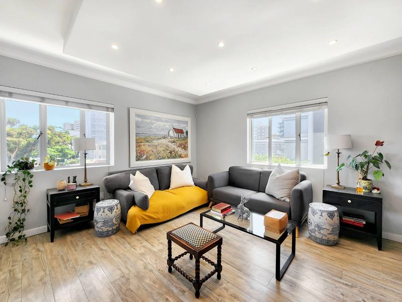 A bright and well-maintained living room featuring recessed ceiling lighting, cove molding, and modern laminate wood flooring with large windows.