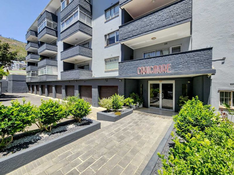 Front exterior view of the Craigmore apartment building, featuring a paved entrance walkway, raised garden beds, and multiple balconies with a modern dark brick finish.