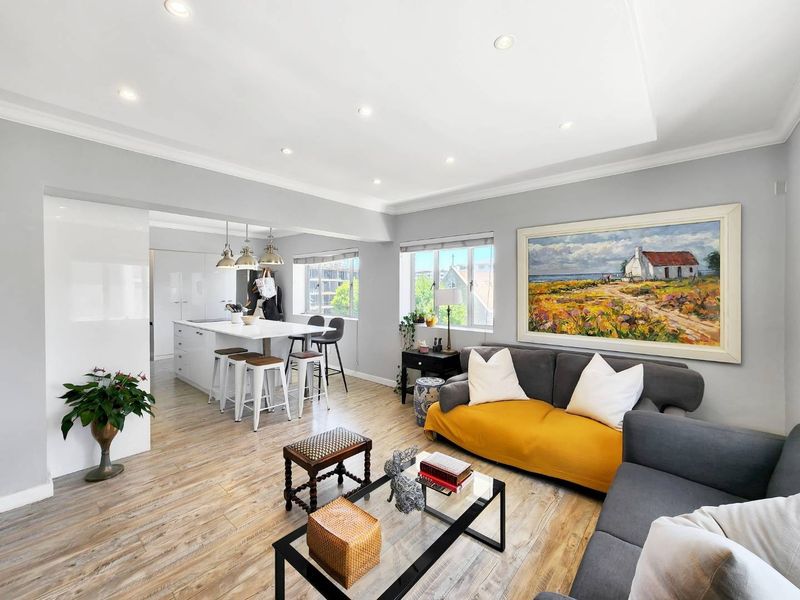 Bright open-plan living and kitchen area featuring modern laminate flooring, recessed lighting, and a functional kitchen island with integrated cabinetry.