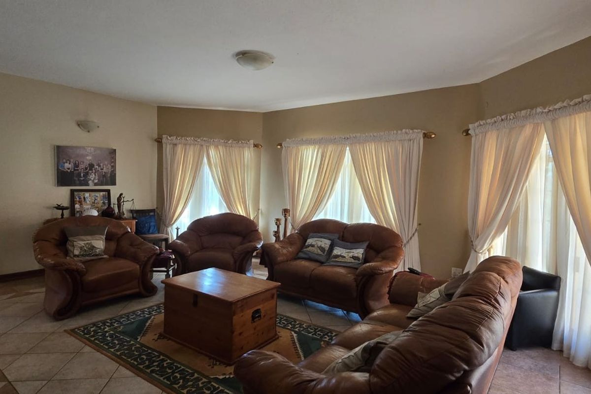 Spacious living room featuring tiled flooring, an arched entryway, and large windows with curtain treatments, offering a comfortable and traditional living space.