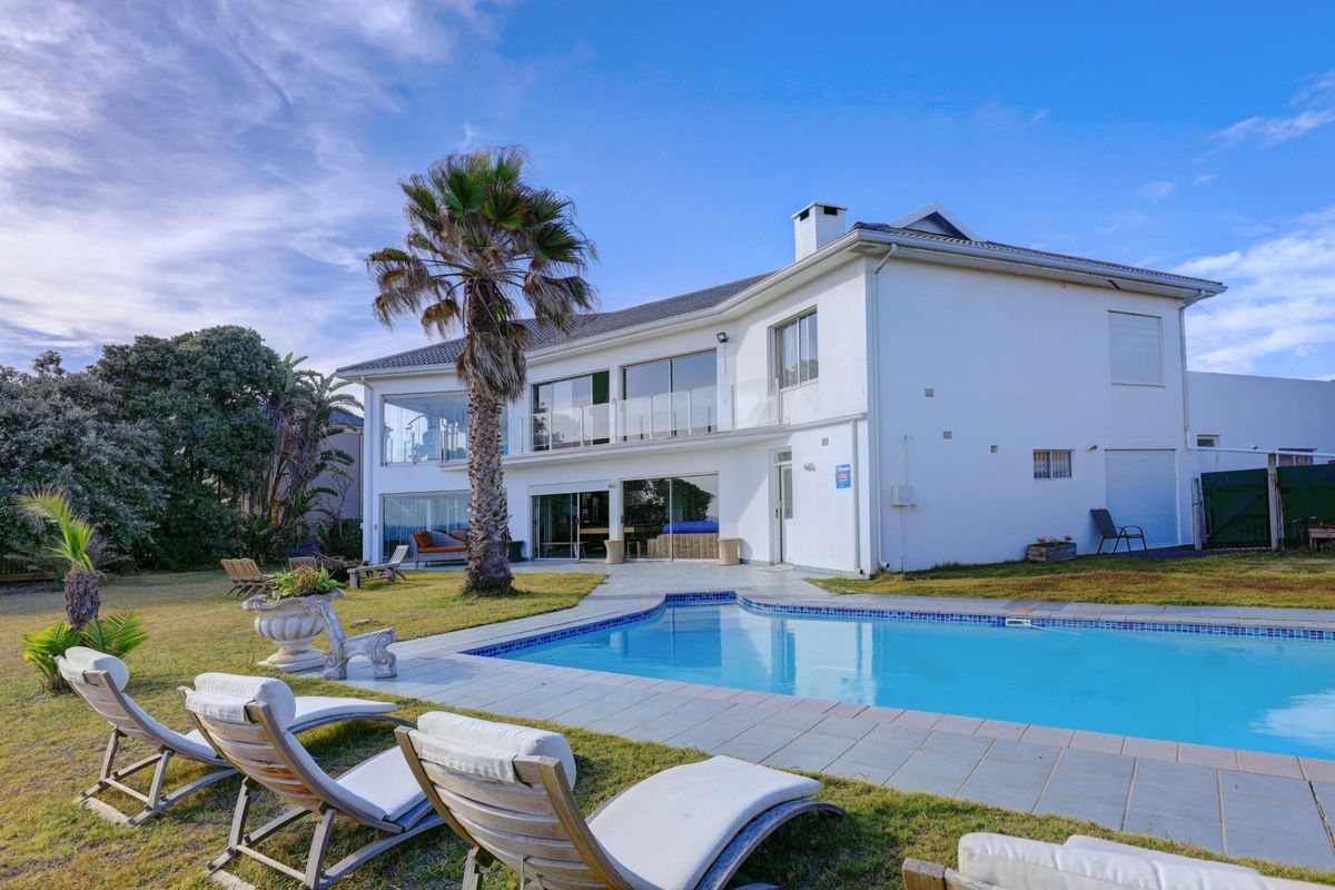 Rear view of a two-story house featuring a swimming pool, landscaped garden, and a spacious upper-level balcony with glass balustrades.